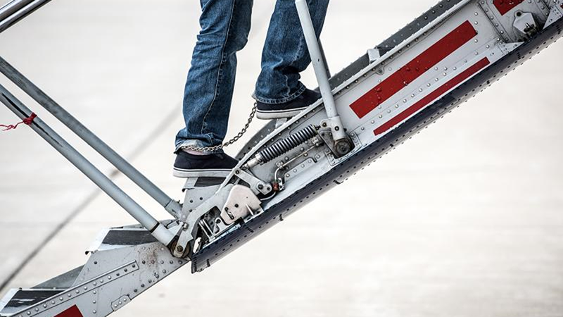 cropped image of shackled feet walking up the stairs to a plane