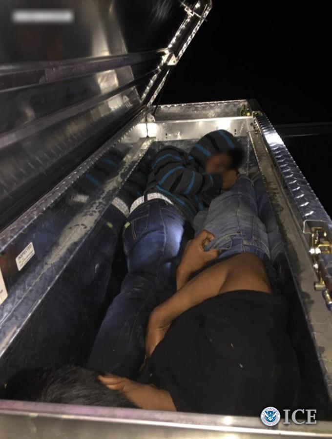 Dos extranjeros indocumentados escondiéndose en la caja de herramientas de una camioneta al ser transportados por contrabandistas tras cruzar la frontera.