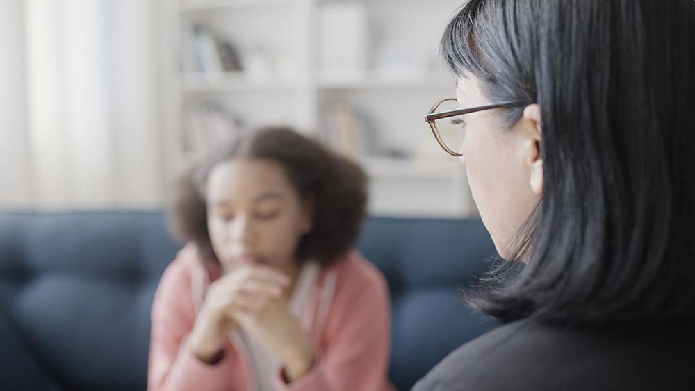 Professional female counselor talking to African American girl, psychotherapy