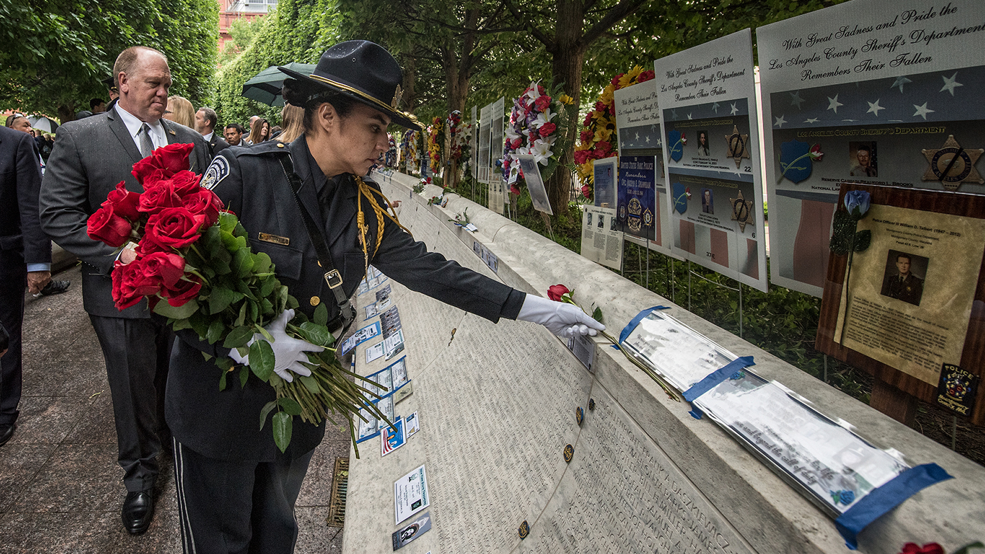 Un miembro de la Guardia de Honor de ICE coloca una rosa sobre el nombre de un oficial caído de ICE. Los miembros de la Guardia de Honor caminan alrededor de todo el Monumento Conmemorativo Nacional de Agentes de la Policía en Washington, D.C.
