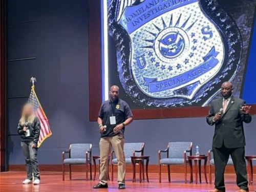 Individuals on a stage presenting with a HSI badge in the background