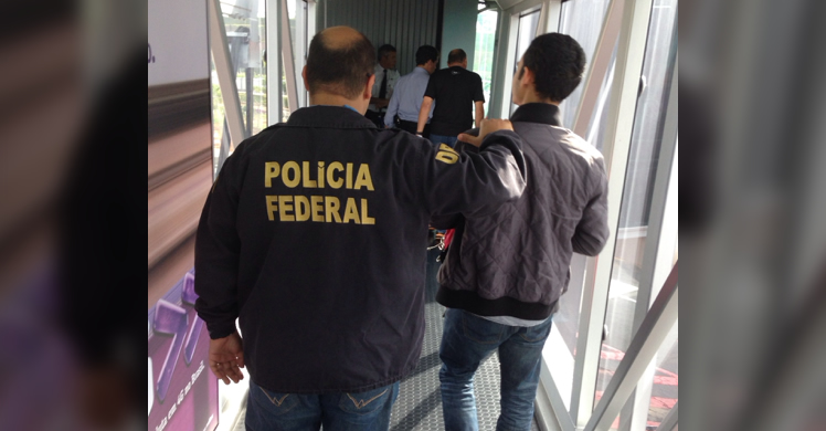 A Brazilian Federal Police officer escorts the attempted murder suspect off of the plane